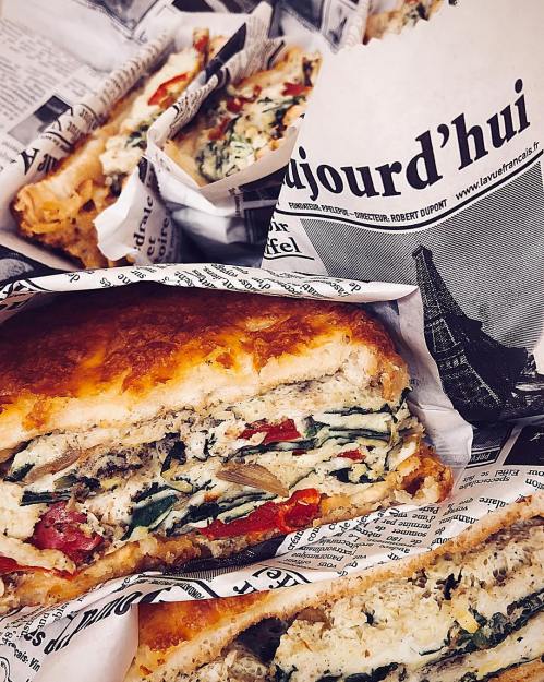 A close-up of layered sandwiches filled with vegetables, wrapped in newspaper print, showcasing a delicious meal.