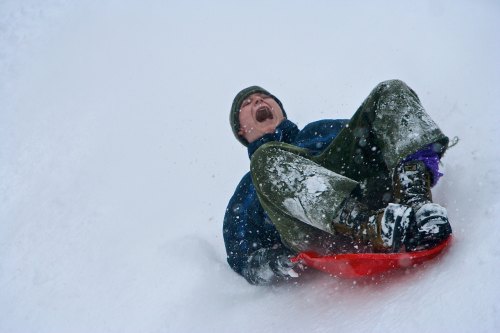 A person joyfully sledding down a snowy hill, laughing as snowflakes swirl around them.