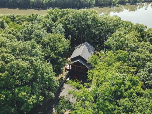 Aerial view of a house surrounded by lush green trees near a calm river.