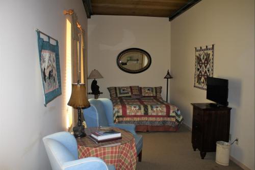 Cozy bedroom with a quilted bedspread, a mirror, a TV, and seating area with blue chairs and a lamp.