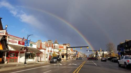 A street scene with shops and a rainbow arching across a cloudy sky.