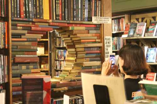 A person takes a photo in a bookstore with a unique archway made of stacked books.