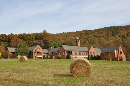 A brick building with a clock tower surrounded by hay bales and autumn foliage on a hillside.