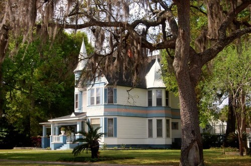 A charming Victorian-style house with a turret, surrounded by lush greenery and draping Spanish moss.