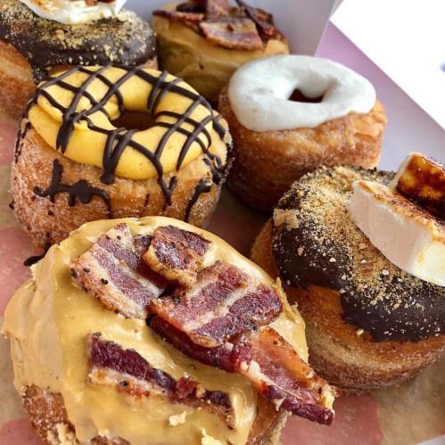 A variety of gourmet donuts topped with chocolate, bacon, and cream, displayed in a box.