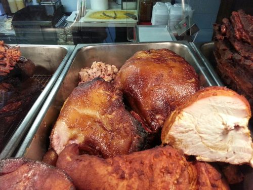 A close-up of various smoked meats, including large pieces of pork and sliced meat, displayed in a food tray.