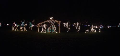 A festive display of illuminated figures depicting a nativity scene in a dark park setting.