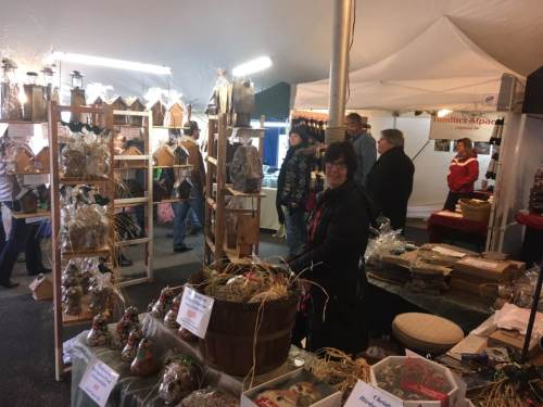 A bustling market scene with vendors and customers, showcasing handmade goods and crafts under a tent.