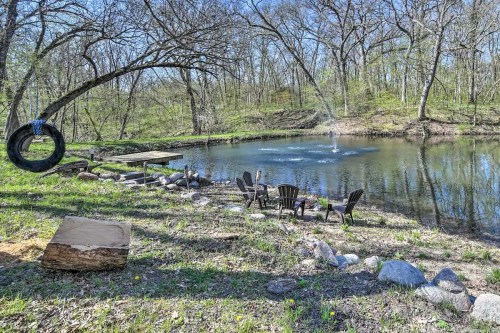 A serene pond surrounded by trees, featuring a tire swing, wooden seating area, and a fountain in the water.