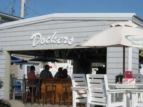 A seaside restaurant named "Dockers" with outdoor seating and umbrellas, featuring patrons enjoying the sunny day.