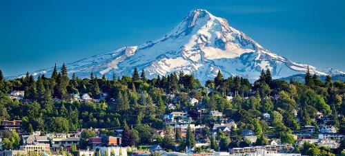 A scenic view of a snow-capped mountain towering over a lush green landscape and a small town below.