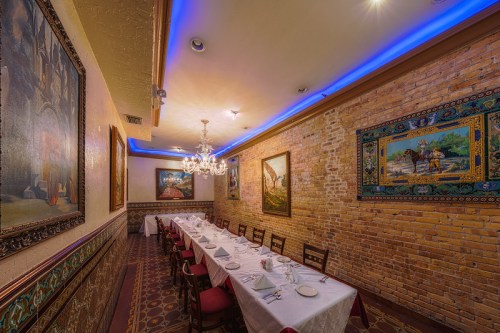 Elegant restaurant interior with a long table, brick walls, colorful artwork, and soft blue lighting.