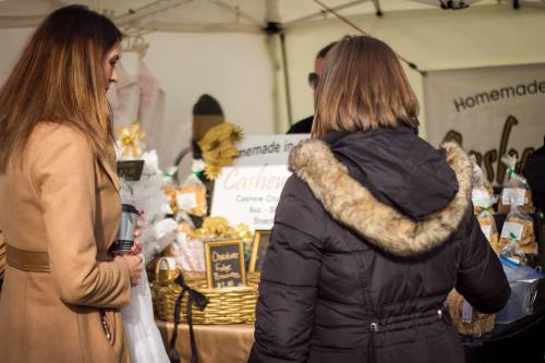 Two women browse a market stall filled with homemade snacks and treats, surrounded by festive decorations.