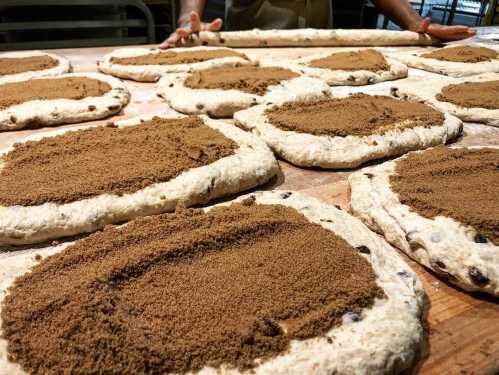 Dough rounds spread with brown sugar on a wooden surface, ready for baking.