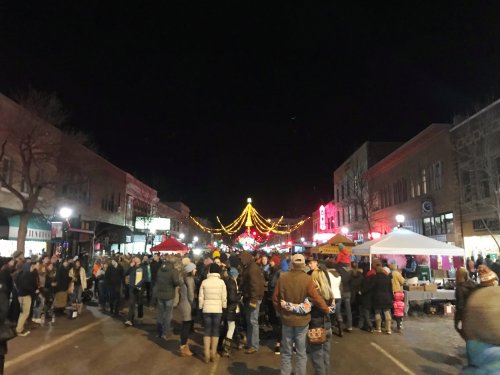 A bustling street at night filled with people, festive lights, and vendor tents during a community event.