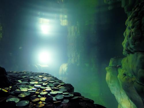 Underwater scene with a rocky surface covered in coins, illuminated by soft, greenish light.