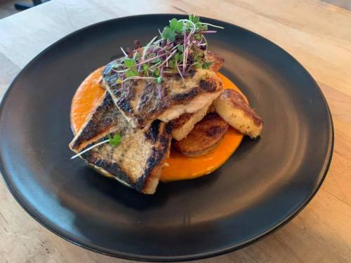 Grilled fish fillet on a bed of orange puree, garnished with microgreens and served with roasted potatoes.
