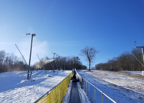 A snowy slope with a conveyor belt for tubing, under a clear blue sky and surrounded by trees.