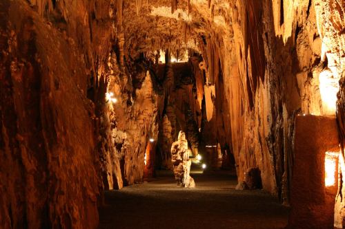 A dimly lit cave with stalactites and stalagmites, featuring warm lighting along the rocky walls.
