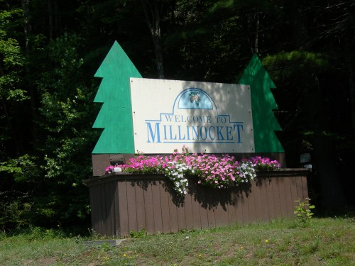 Welcome sign for Millinocket, featuring green trees and colorful flowers at the base.