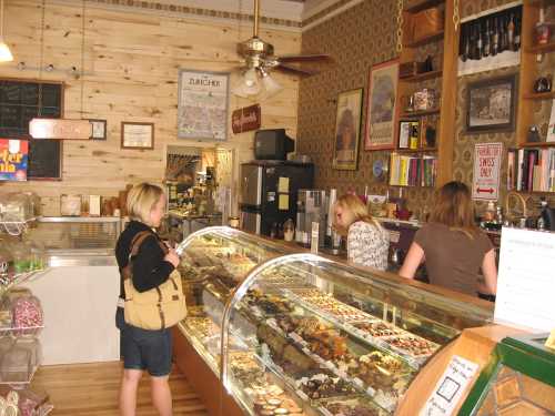 A cozy bakery interior with a glass display case filled with pastries, and customers interacting with staff.