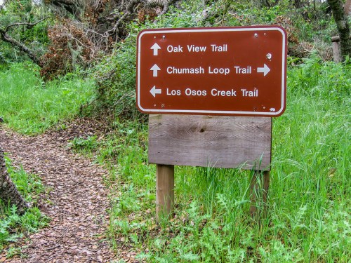 Trail sign with directions for Oak View, Chumash Loop, and Los Osos Creek Trails, surrounded by green foliage.