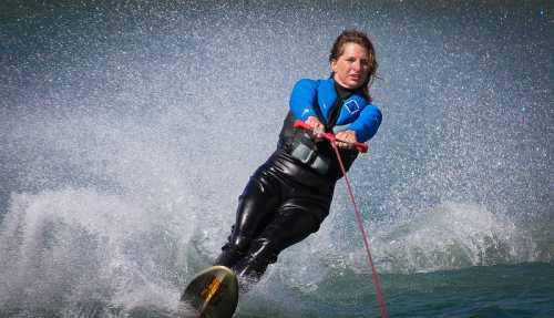 A woman in a wetsuit water skiing, creating splashes as she glides across the water.