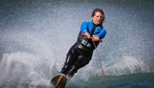 A woman in a wetsuit water skiing, creating splashes as she glides across the water.