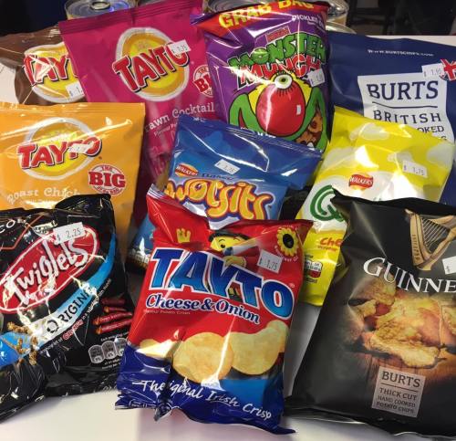A variety of snack bags, including crisps and chips, displayed on a table with price tags visible.