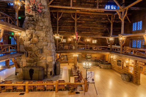 Interior of a rustic lodge featuring a large stone fireplace, wooden beams, and cozy seating areas.