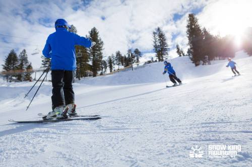 Three skiers in blue jackets navigate a snowy slope under a bright sky at Snow King Mountain.