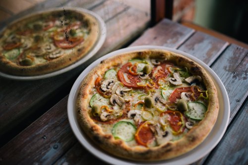 A freshly baked pizza topped with tomatoes, mushrooms, and green peppers, resting on a wooden table.