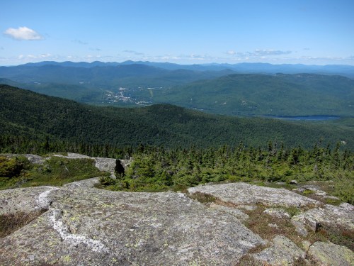 A panoramic view of lush green mountains and valleys under a clear blue sky, with rocky foreground.