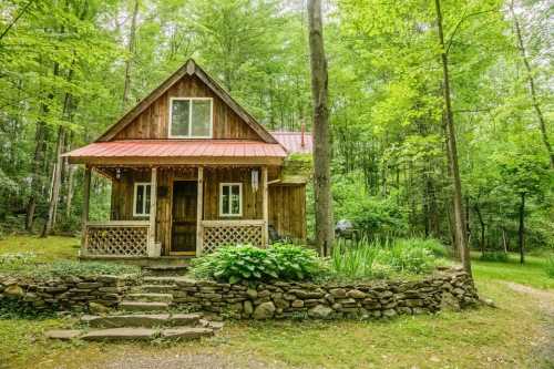 A charming wooden cabin with a red roof, surrounded by lush green trees and a stone pathway.