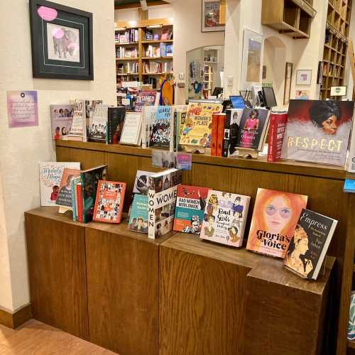 A wooden display featuring various books on women's empowerment and notable figures in a cozy bookstore setting.