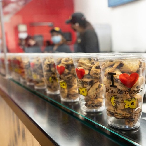 A row of clear cups filled with cookies, labeled "I ❤️ mac & cheese," on a counter in a restaurant.