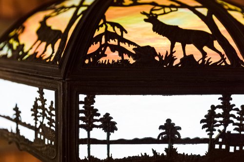A decorative lamp featuring silhouettes of animals and trees against a colorful sunset background.