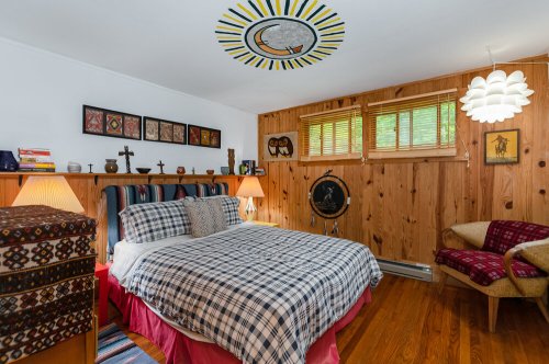Cozy bedroom with a checkered bedspread, wooden walls, artwork, and warm lighting from lamps and a unique ceiling design.
