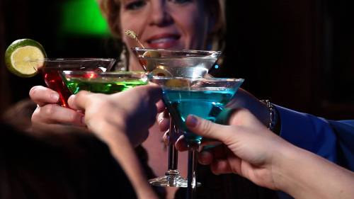 A group of people toasting with colorful cocktails in a dimly lit setting.
