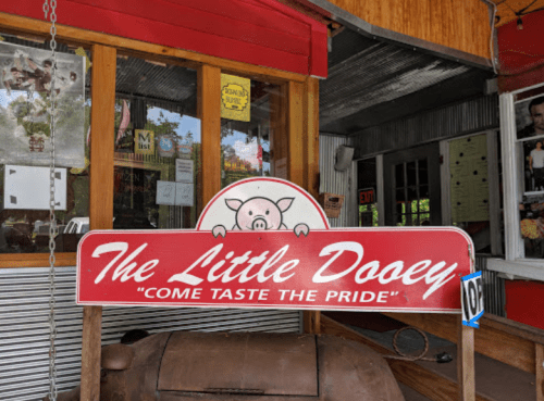 Sign for "The Little Dooey" restaurant featuring a pig graphic and the slogan "Come Taste the Pride."