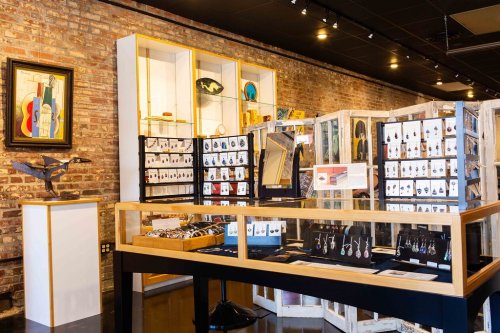 Display of jewelry and art in a modern gallery with brick walls and wooden showcases.