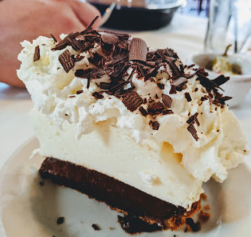 A slice of chocolate cream pie topped with whipped cream and chocolate shavings on a plate.