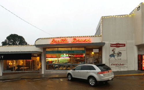 A diner with neon signage reading "Brett's Diner," featuring a gray car parked outside on a rainy day.