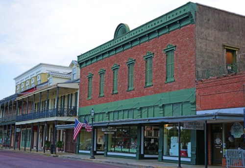 Historic buildings with green accents and American flags line a charming street in a small town.