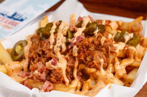 A plate of loaded fries topped with pulled pork, jalapeños, and drizzled with sauce.