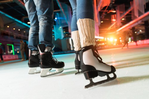 Two pairs of ice skates on an ice rink, with colorful lights in the background.