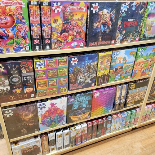 A colorful display of various puzzle boxes, including themes like cartoons, music, and video games on wooden shelves.
