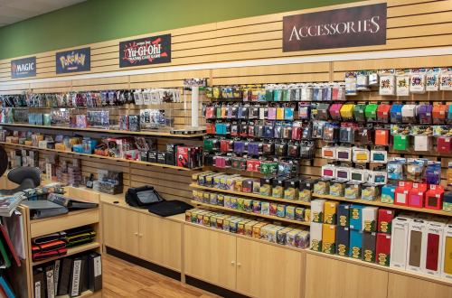 A store display featuring various trading card games and accessories on shelves, including Magic, Pokémon, and Yu-Gi-Oh!