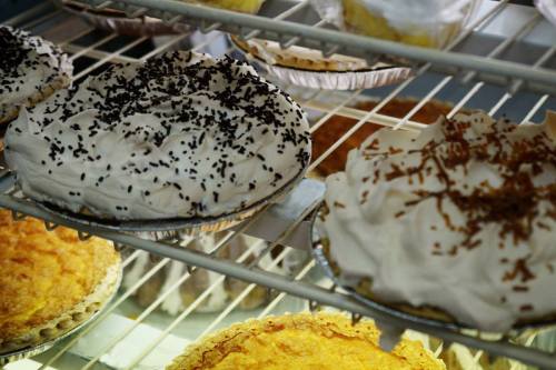 A display of various pies, featuring whipped cream toppings and decorative sprinkles, in a glass case.