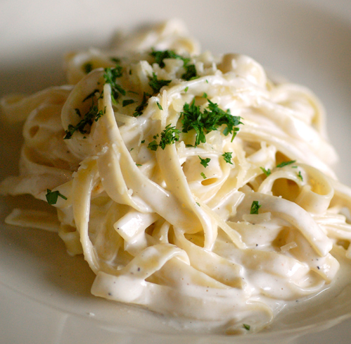 A close-up of fettuccine pasta topped with creamy sauce and sprinkled with fresh parsley.